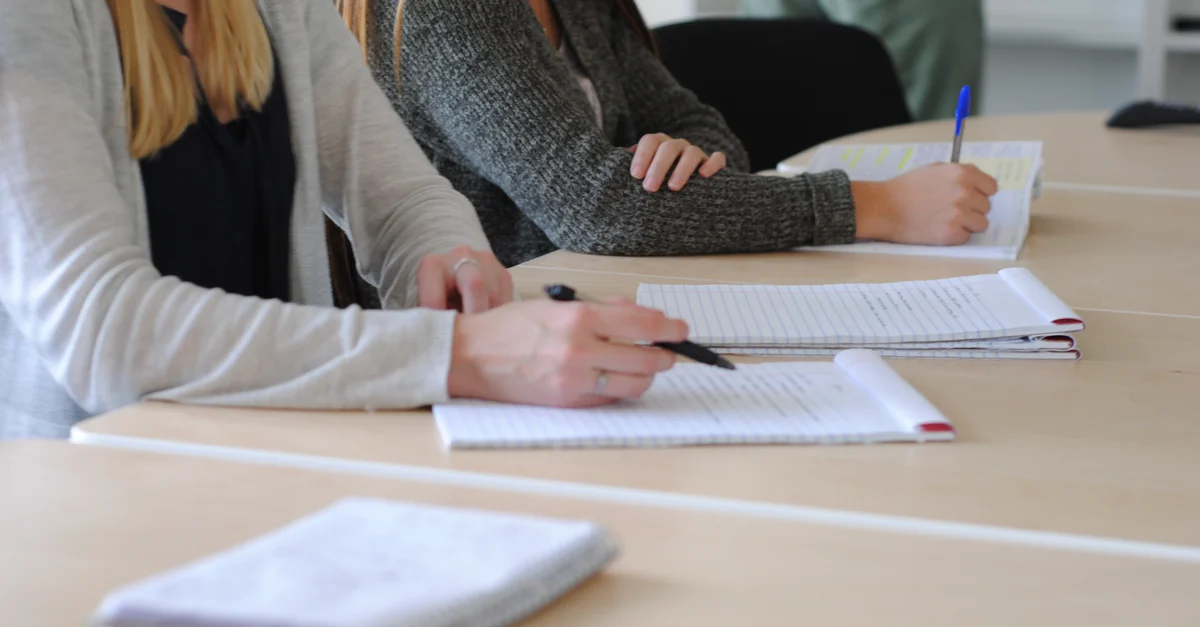 Groupe d'étudiants prenant des notes lors d'une réunion dans une salle de classe bien éclairée.