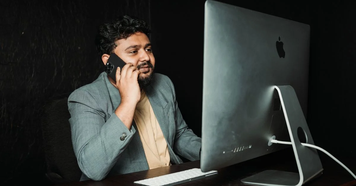 Homme professionnel multitâche au bureau utilisant un ordinateur et un smartphone.