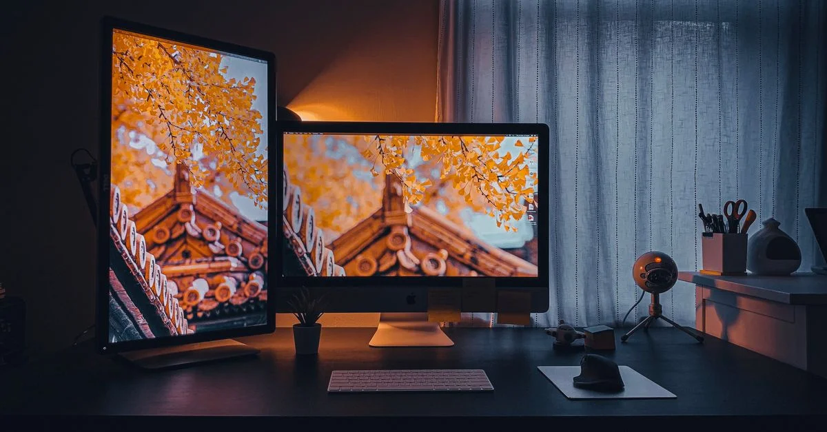 Configuration de bureau à domicile confortable avec des écrans doubles affichant un paysage automnal.