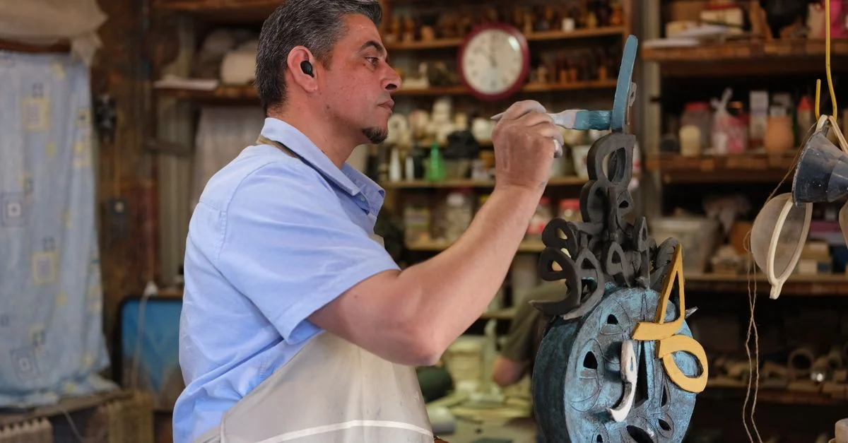 Un artisan qualifié peint méticuleusement une sculpture dans son atelier, entouré d'outils et de matériaux.