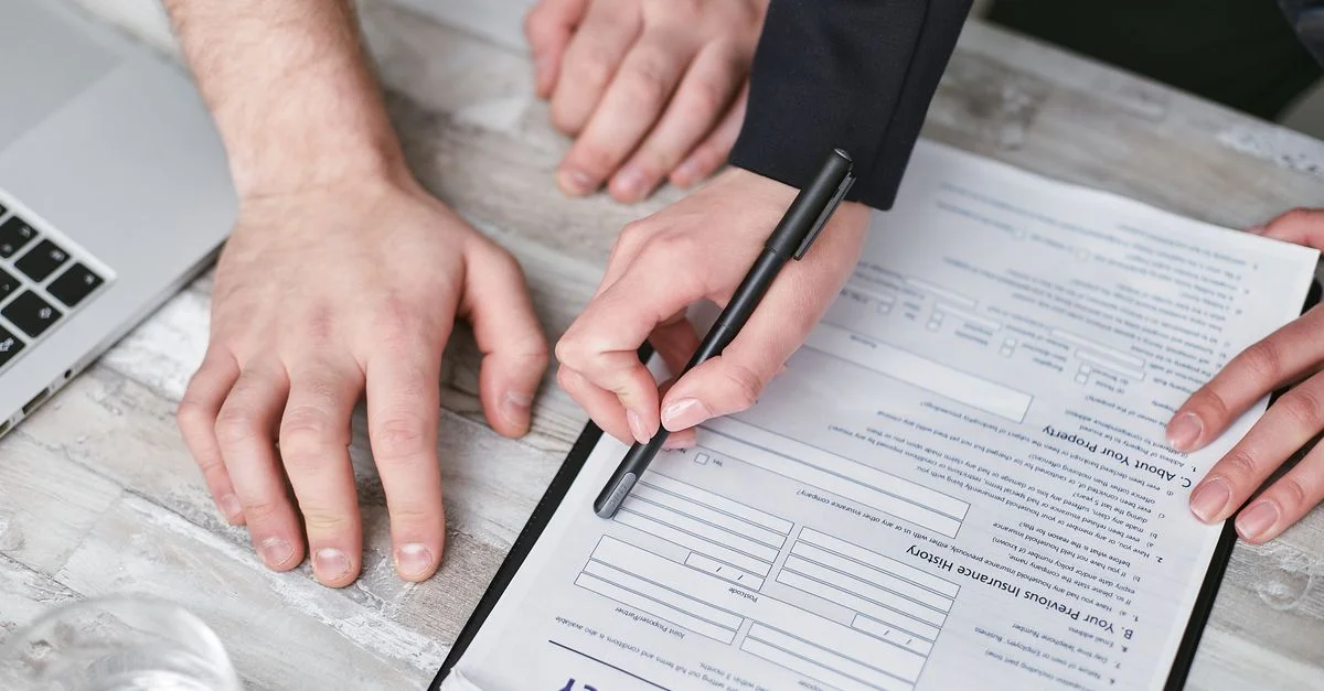 Image en gros plan de deux personnes signant un document de police d'assurance sur un bureau en bois.