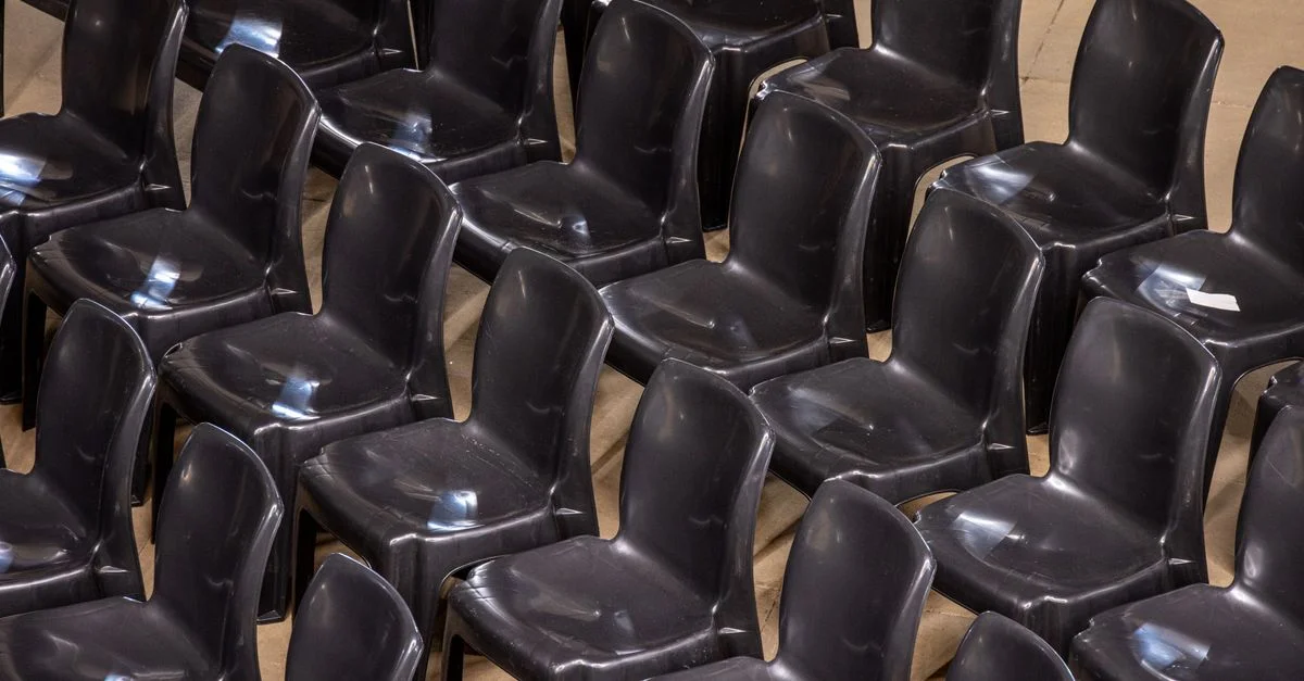 Plusieurs rangées de chaises vides en plastique noir, alignées à l'intérieur pour l'aménagement d'un événement.