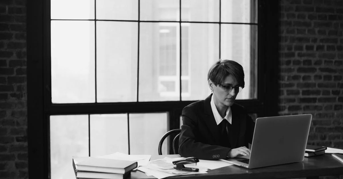 Photo en noir et blanc d'une femme travaillant sur un ordinateur portable dans un cadre de bureau.