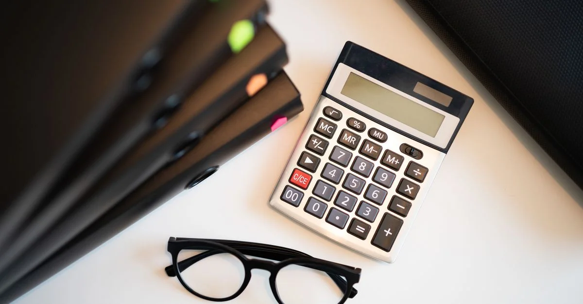 Calculatrice avec des lunettes et des dossiers sur un bureau. Parfait pour les thèmes de finance et de comptabilité.