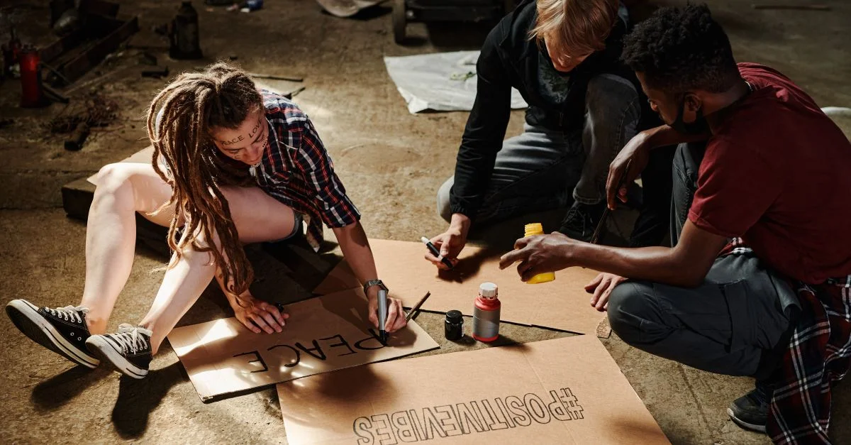 Trois jeunes activistes créant des panneaux de protestation à l'intérieur sur du carton, favorisant la paix et la positivité.