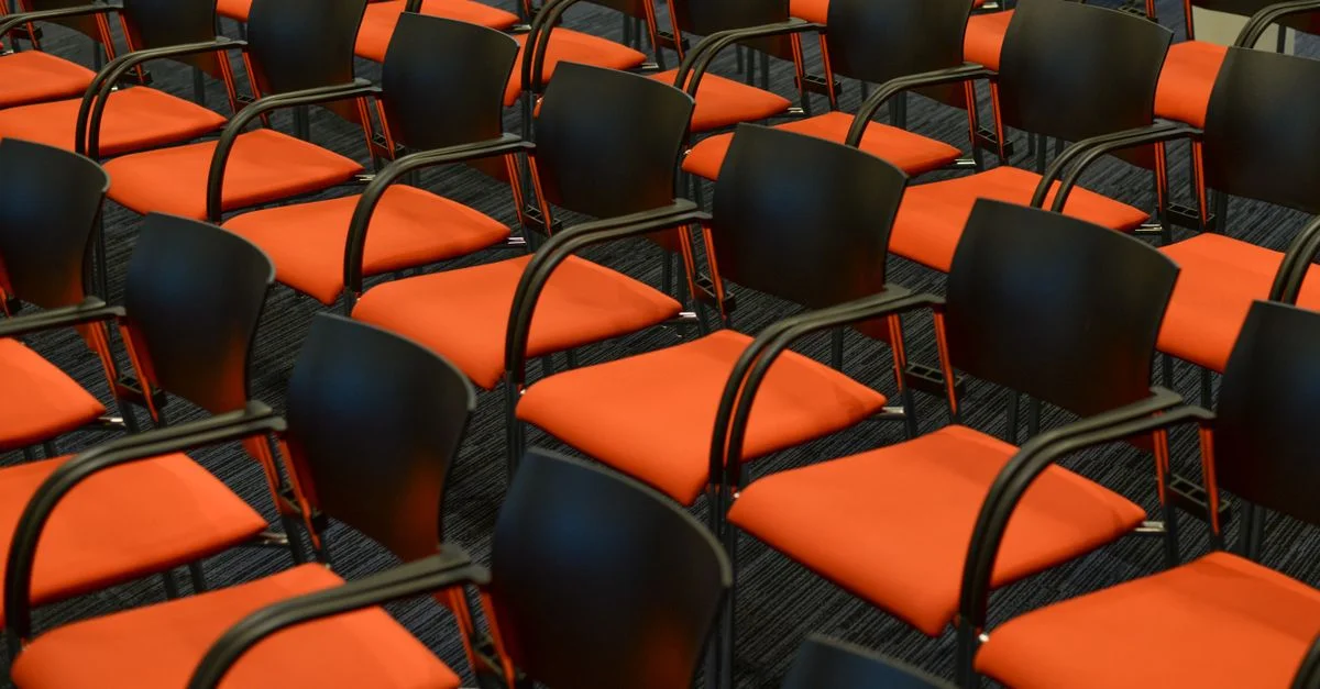 Un auditorium moderne avec des rangées de chaises noires et orange vides, prêtes pour un événement.