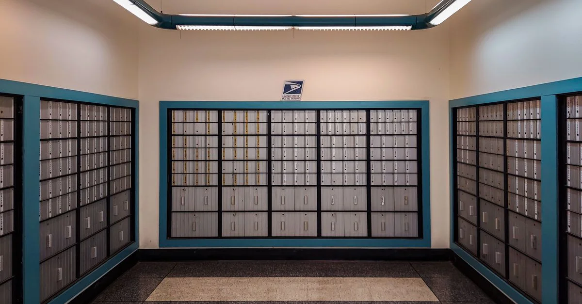 Rangées de boîtes aux lettres verrouillées dans un intérieur de bureau de poste avec un éclairage suspendu.