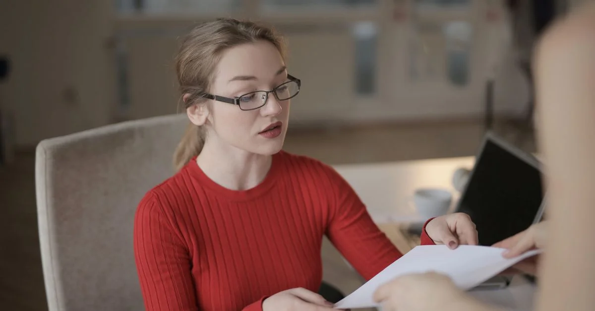 Femme caucasienne en pull rouge recevant un document dans un bureau bien éclairé.