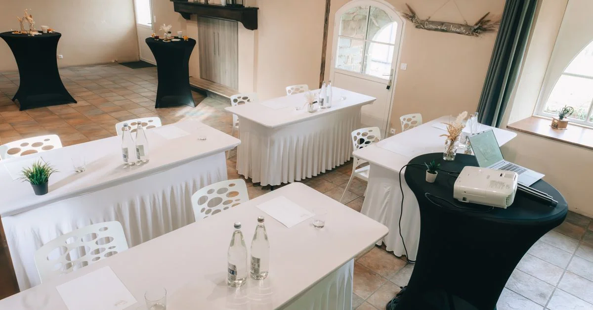 Salle de réunion spacieuse avec des tables élégantes recouvertes de lin, des chaises et un projecteur prêt pour les présentations.