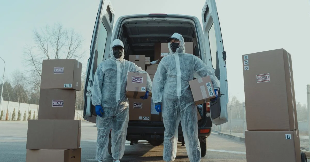 Deux livreurs en équipement de protection chargent des boîtes dans une camionnette à l'extérieur, garantissant une manipulation sûre des colis.